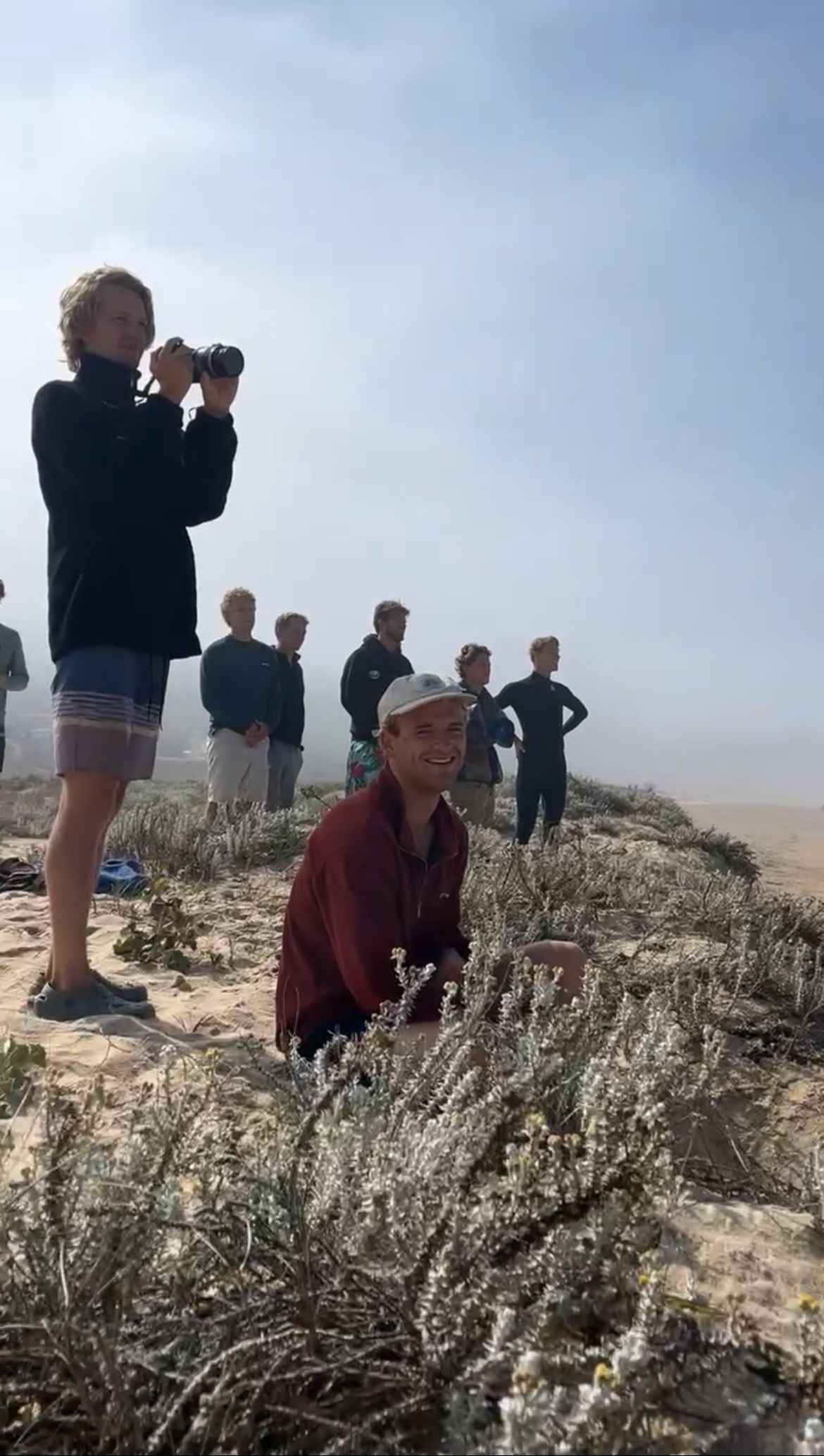 Friends on a foggy beach with a camera, surf wetsuits.