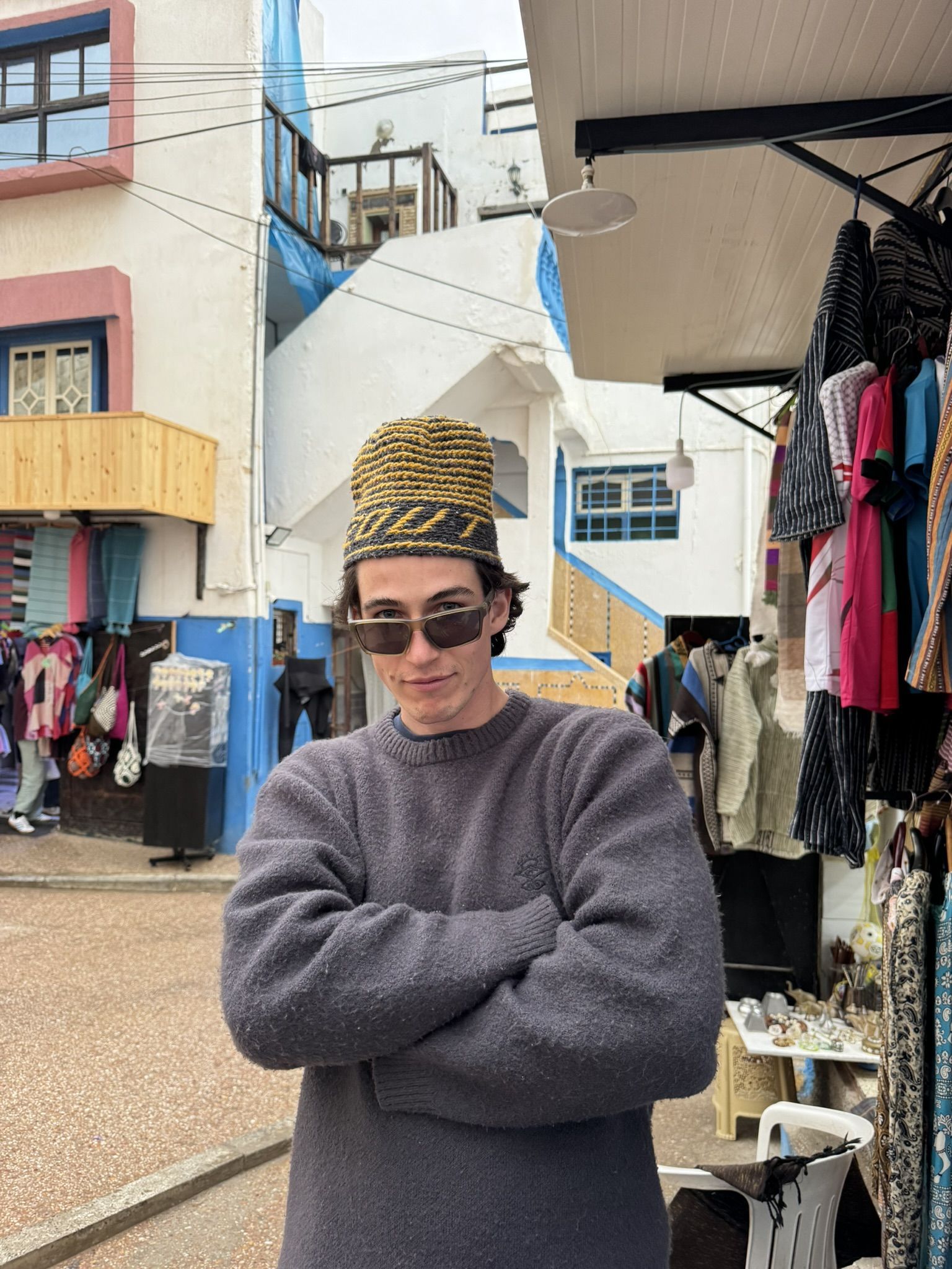 Tom in a Moroccan street market, traditional knit hat, colourful stalls behind.
