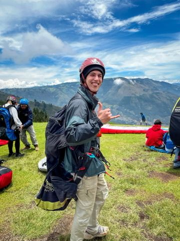 Tom in paragliding gear with helmet, harness and a shaka — Andes behind.