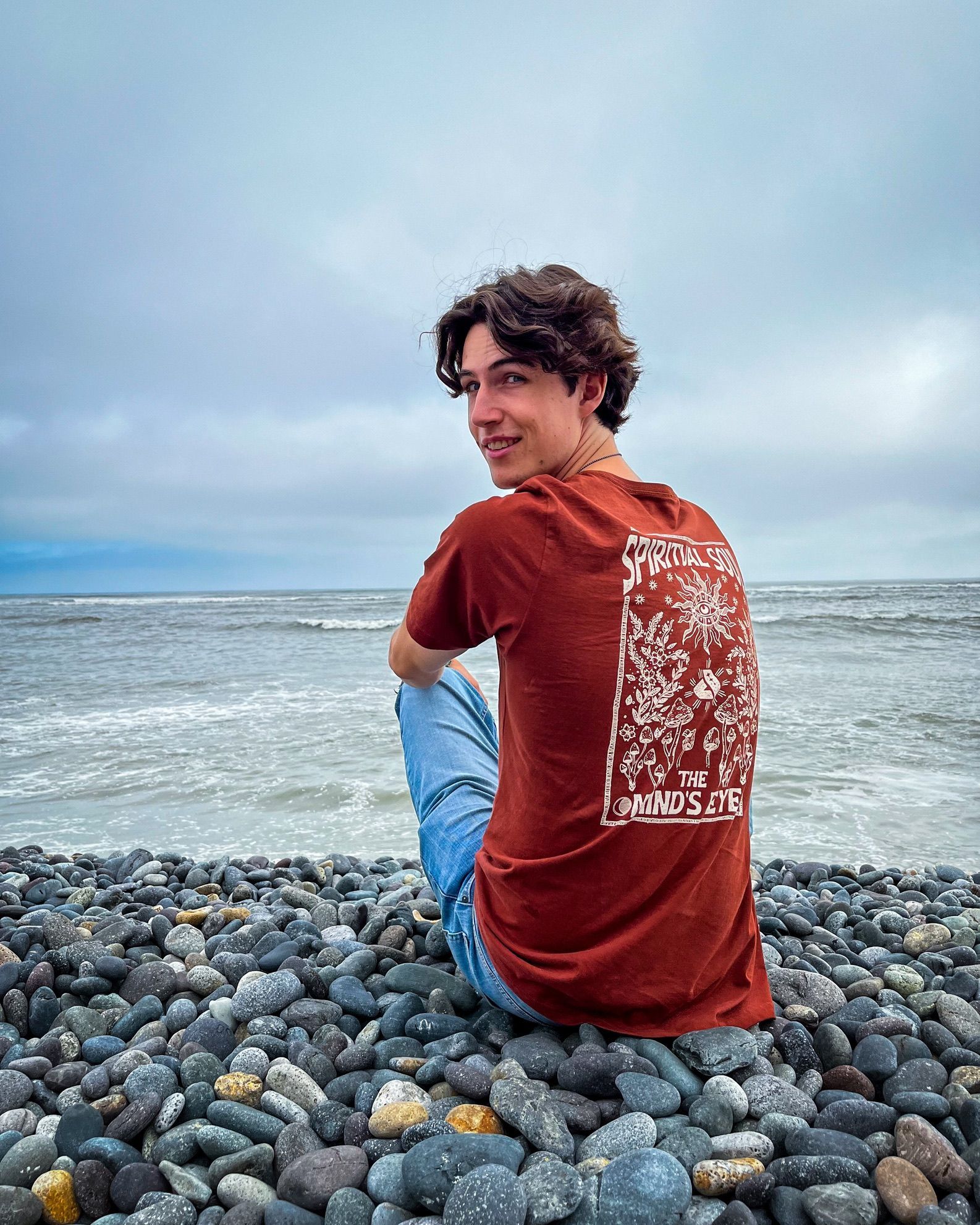 Portrait on a pebble beach, looking over the shoulder toward the sea.