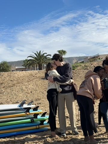 At a surf camp, surfboards lined up, palms behind — a quiet moment with a partner.