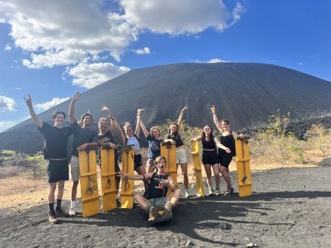 Group of friends with sand-boards in front of a black volcano in Nicaragua.