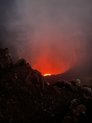 A volcano crater glowing with lava at twilight, smoke rising.