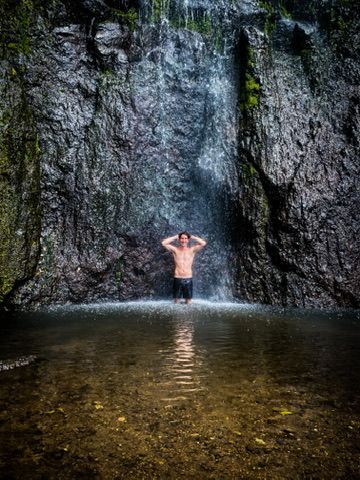 Tom under a waterfall in the jungle.