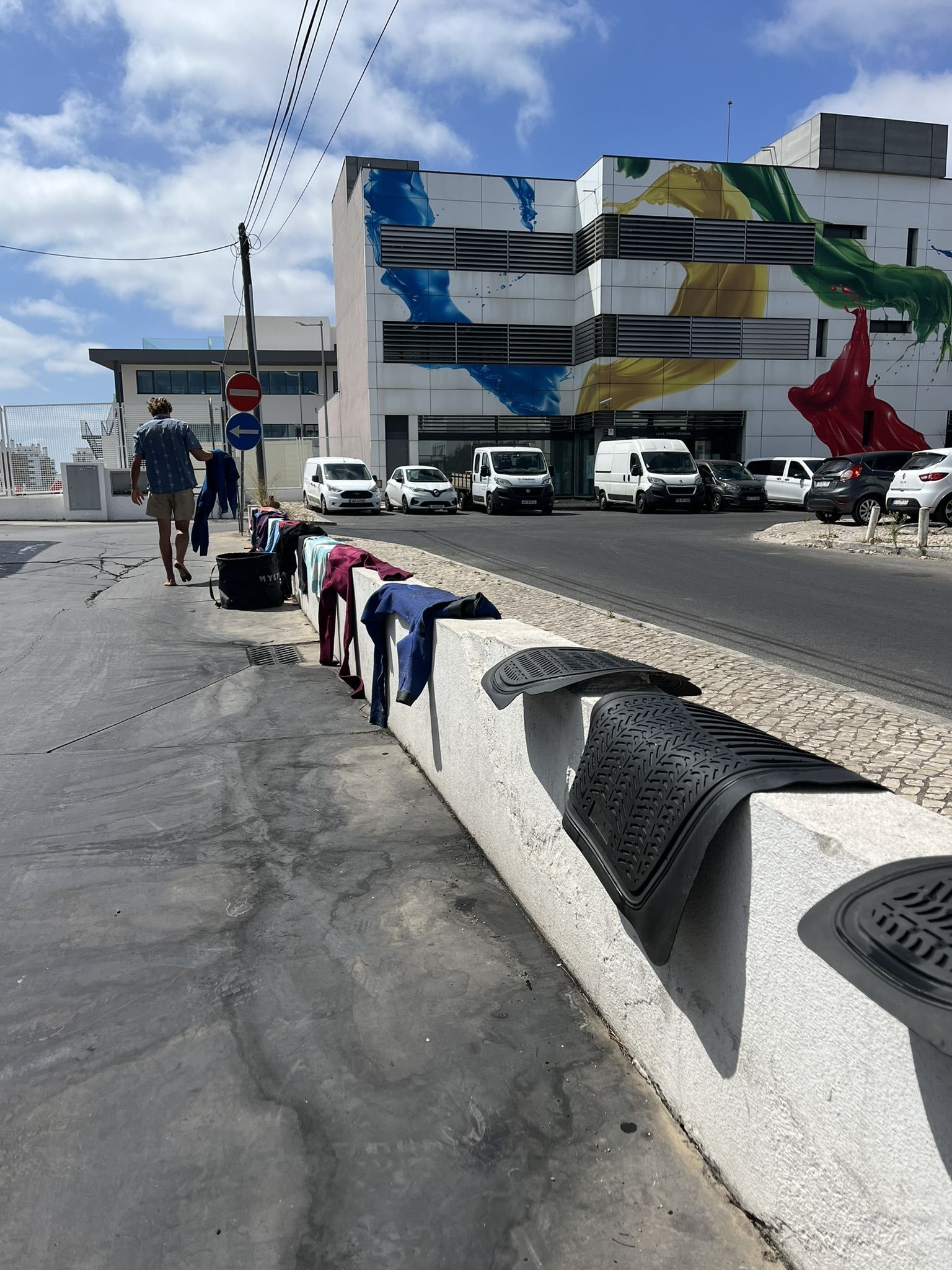 Wetsuits drying on a street barrier under coastal sun.